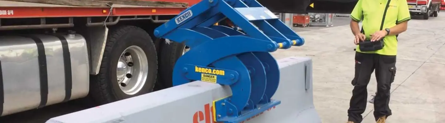 Worker observing as heavy machinery moves a concrete safety barrier into place on a roadway construction site.